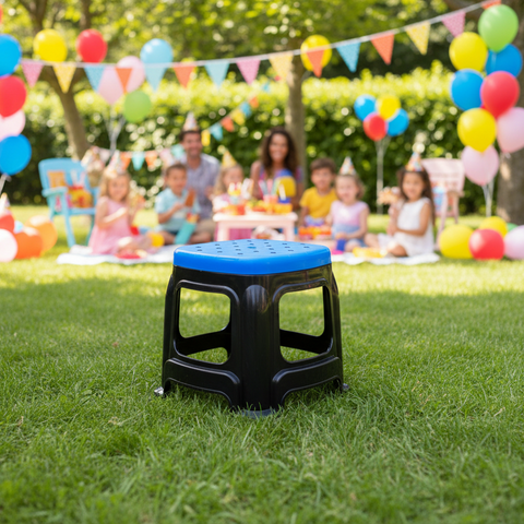 Black stool with blue top on grass in front of a colorful outdoor birthday party.