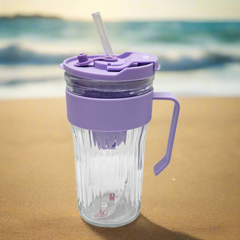 Clear tumbler with purple lid and handle on a sandy beach
