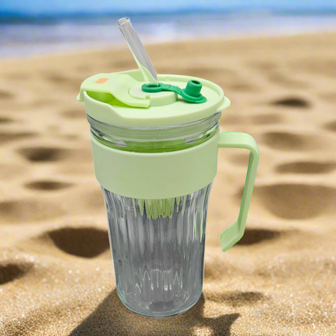 Clear tumbler with green lid and handle on a sandy beach